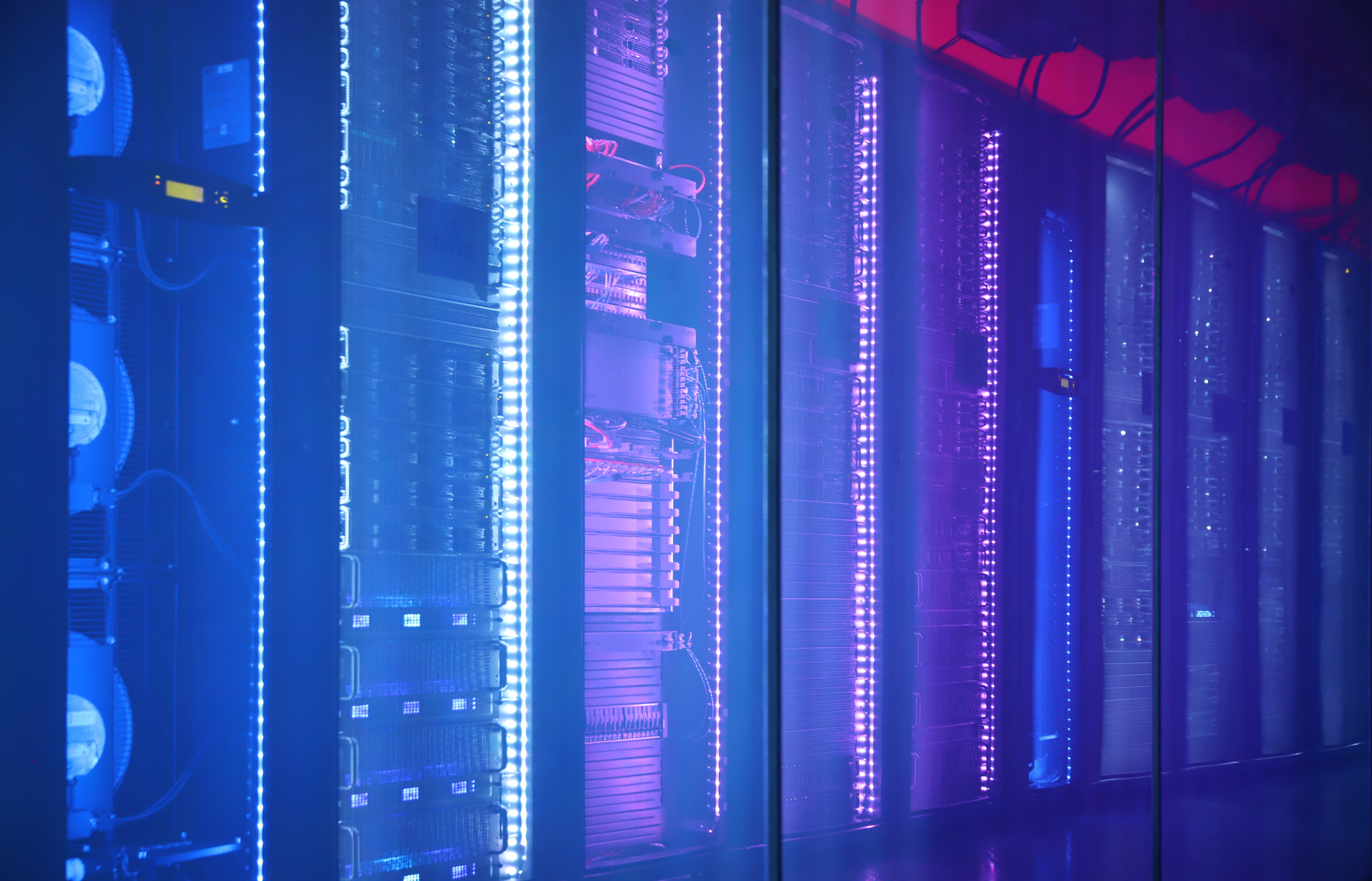 TERRA CLOUD Cube Reihe von Serverracks in einem Rechenzentrum, beleuchtet mit blauem und violettem LED-Licht hinter einer Glaswand