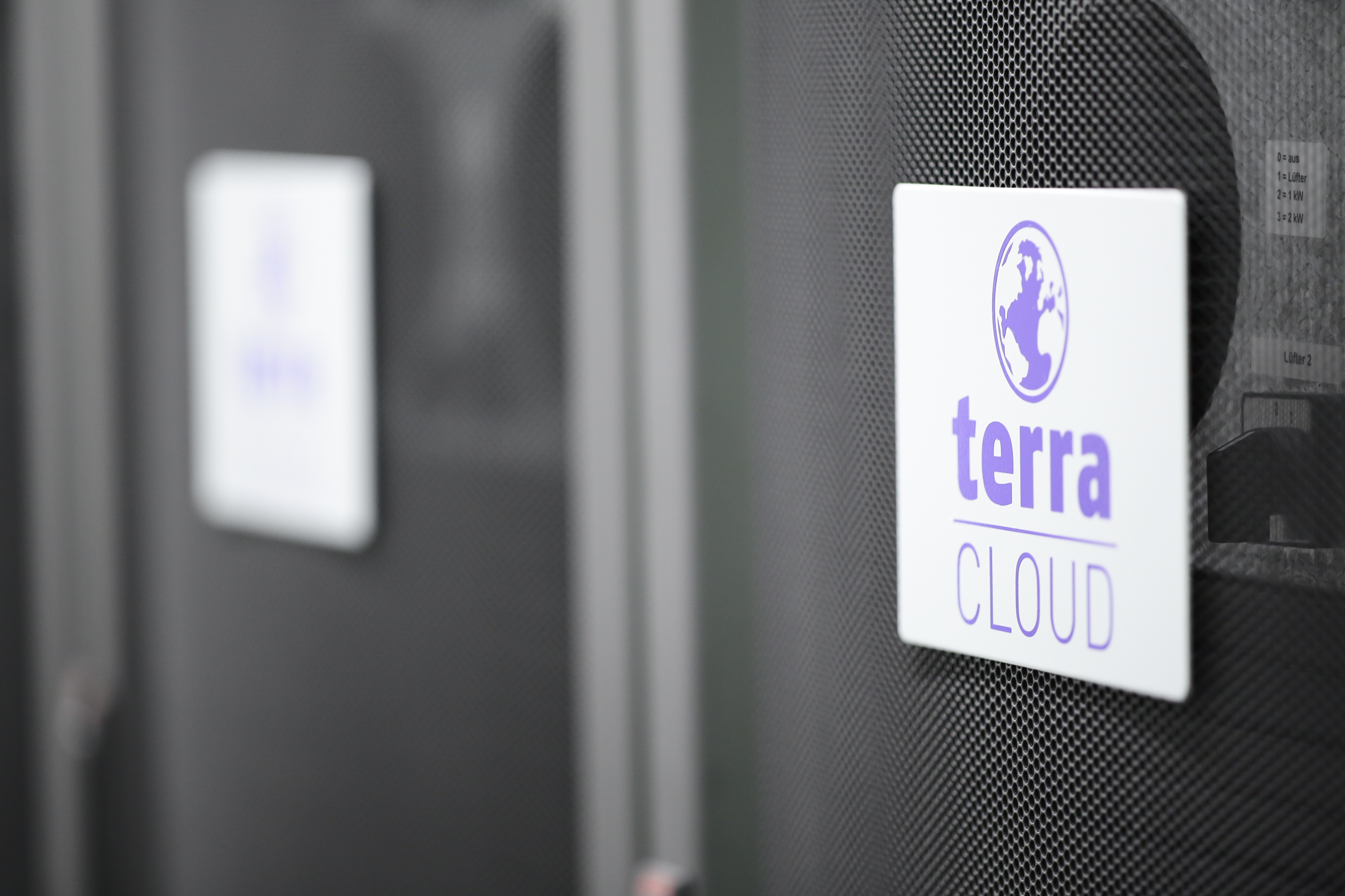 TERRA CLOUD Server Nahaufnahme eines Serverracks mit dem Logo 'terra CLOUD' auf einem weißen Schild, befestigt an einer gelochten schwarzen Frontabdeckung