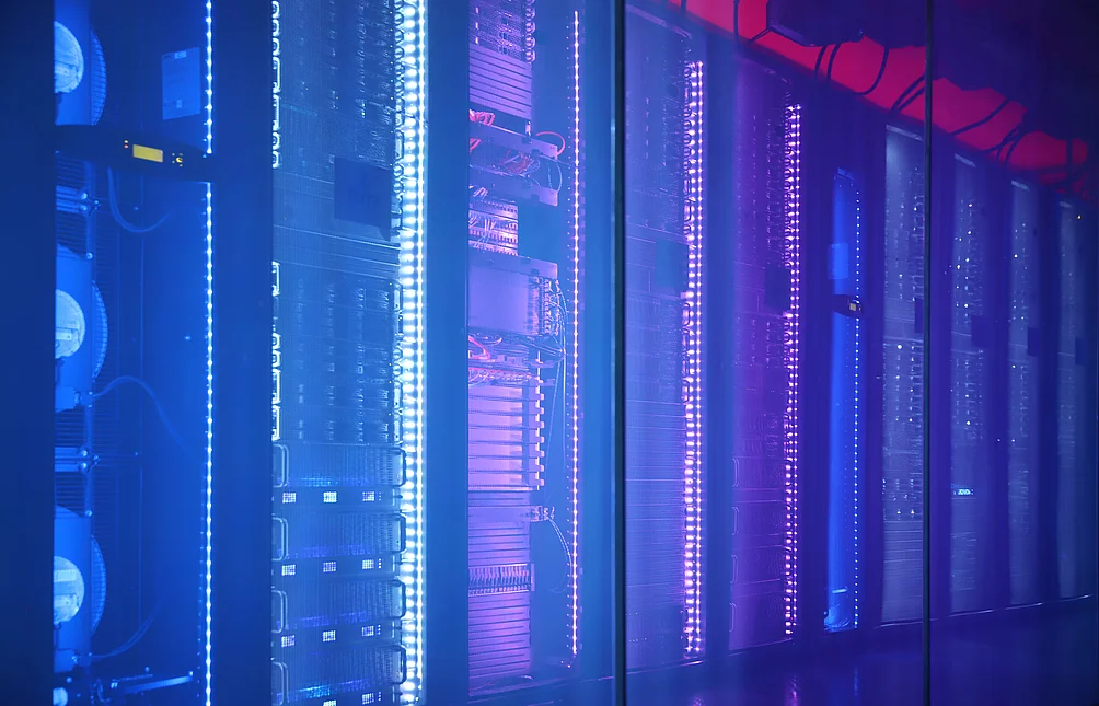 Reihe von Serverracks in einem Rechenzentrum, beleuchtet mit blauem und violettem LED-Licht hinter einer Glaswand