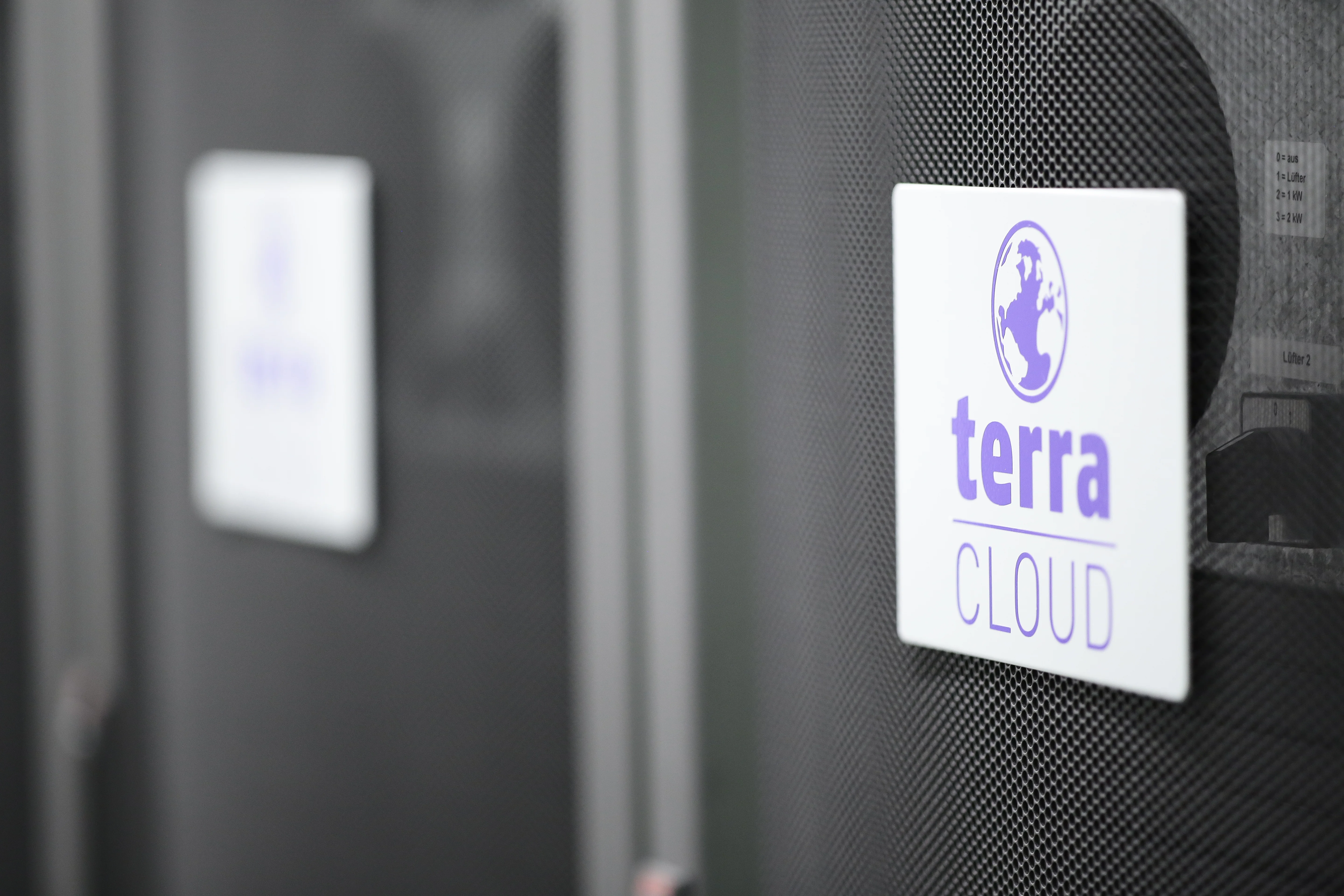 Nahaufnahme eines Serverracks mit dem Logo 'terra CLOUD' auf einem weißen Schild, befestigt an einer gelochten schwarzen Frontabdeckung