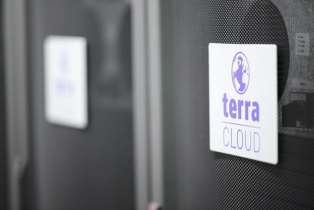 TERRA CLOUD Server Nahaufnahme eines Serverracks mit dem Logo 'terra CLOUD' auf einem weißen Schild, befestigt an einer gelochten schwarzen Frontabdeckung
