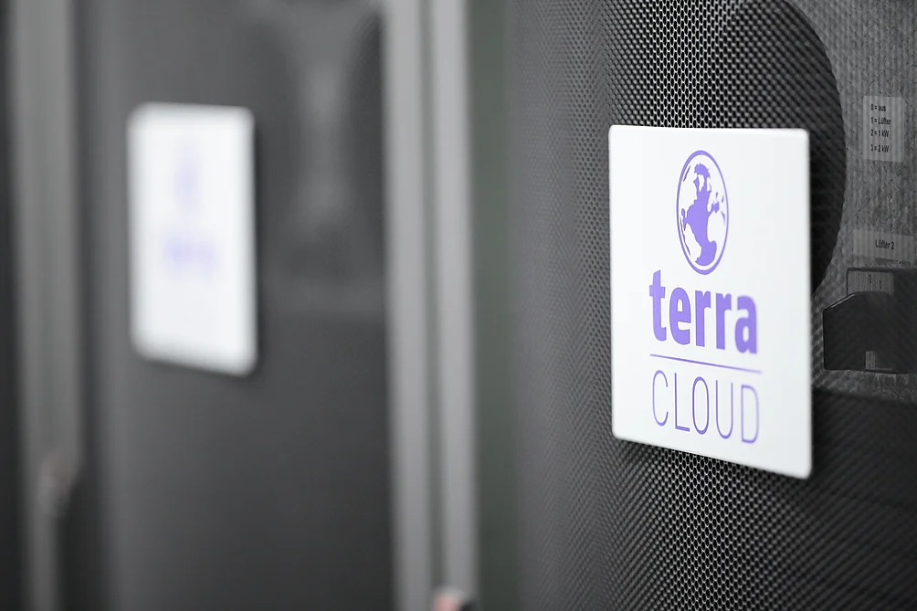Nahaufnahme eines Serverracks mit dem Logo 'terra CLOUD' auf einem weißen Schild, befestigt an einer gelochten schwarzen Frontabdeckung