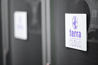 TERRA CLOUD Server Nahaufnahme eines Serverracks mit dem Logo 'terra CLOUD' auf einem weißen Schild, befestigt an einer gelochten schwarzen Frontabdeckung